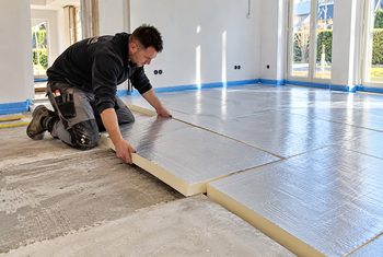 Monteur legt PIR-isolatieplaten met een reflecterende folielaag op een betonnen vloer