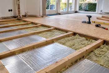 Houten vloer met minerale wol en reflecterende isolatiefolie tussen de vloerbalken tijdens het aanbrengen van vloerisolatie