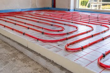 Vloerisolatie met vloerverwarming en reflecterende isolatieplaten Rode vloerverwarmingsbuizen aangelegd op isolatieplaten met een reflecterende folielaag